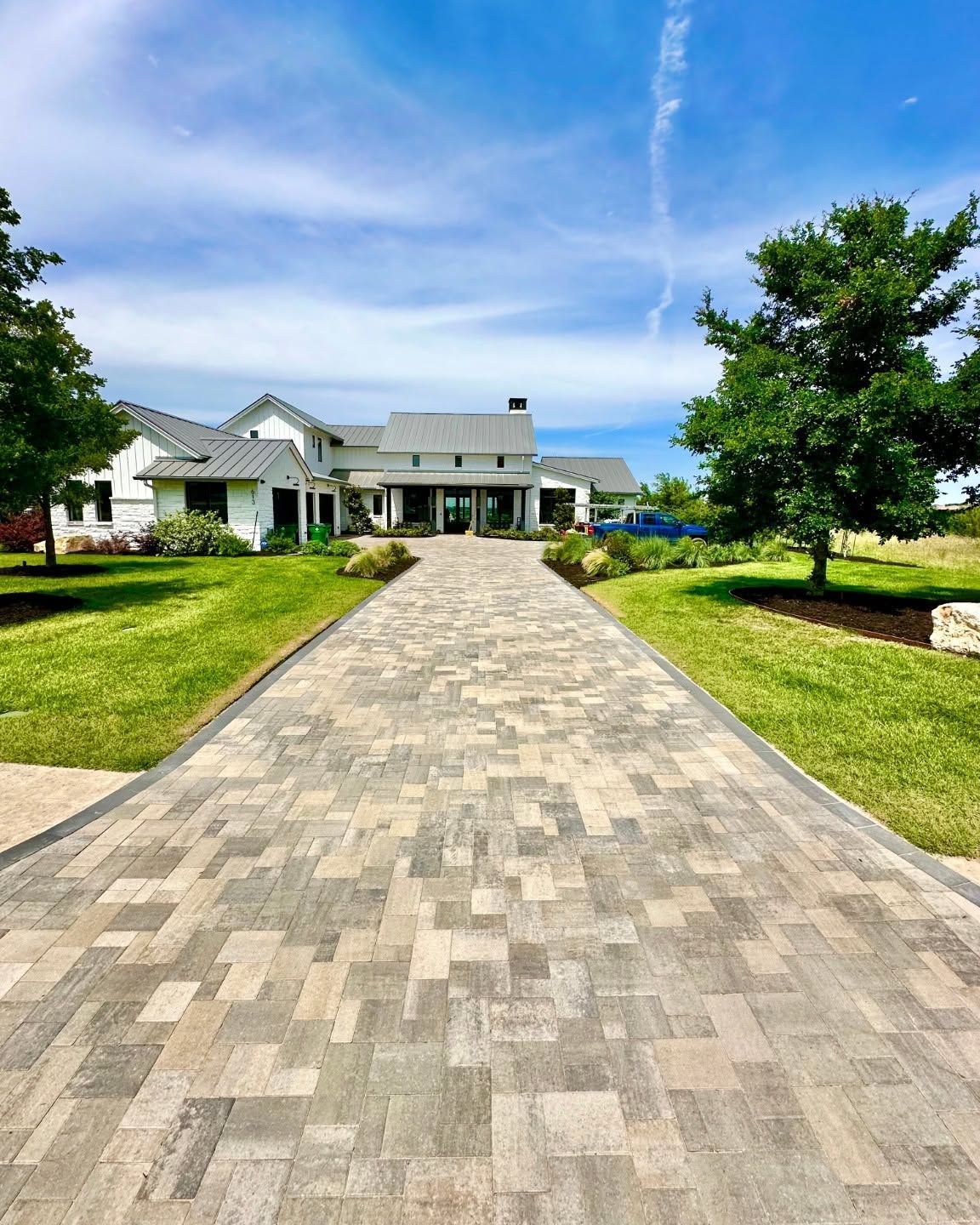 Stone walkway leading to a white house with green lawn and trees under a blue sky