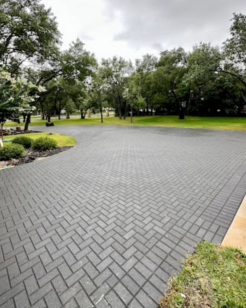 Wet gray brick driveway beside a green park with trees and grass after rain