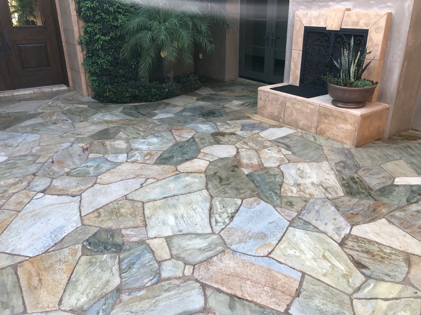 Stone-tiled courtyard with a doorway, potted plant, and low planter against a stucco wall