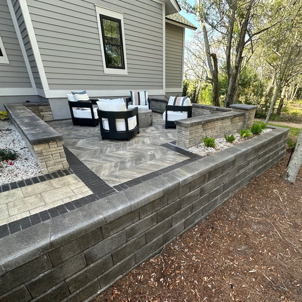 Backyard patio with gray pavers, built-in stone seating, and black-and-white outdoor furniture beside a house