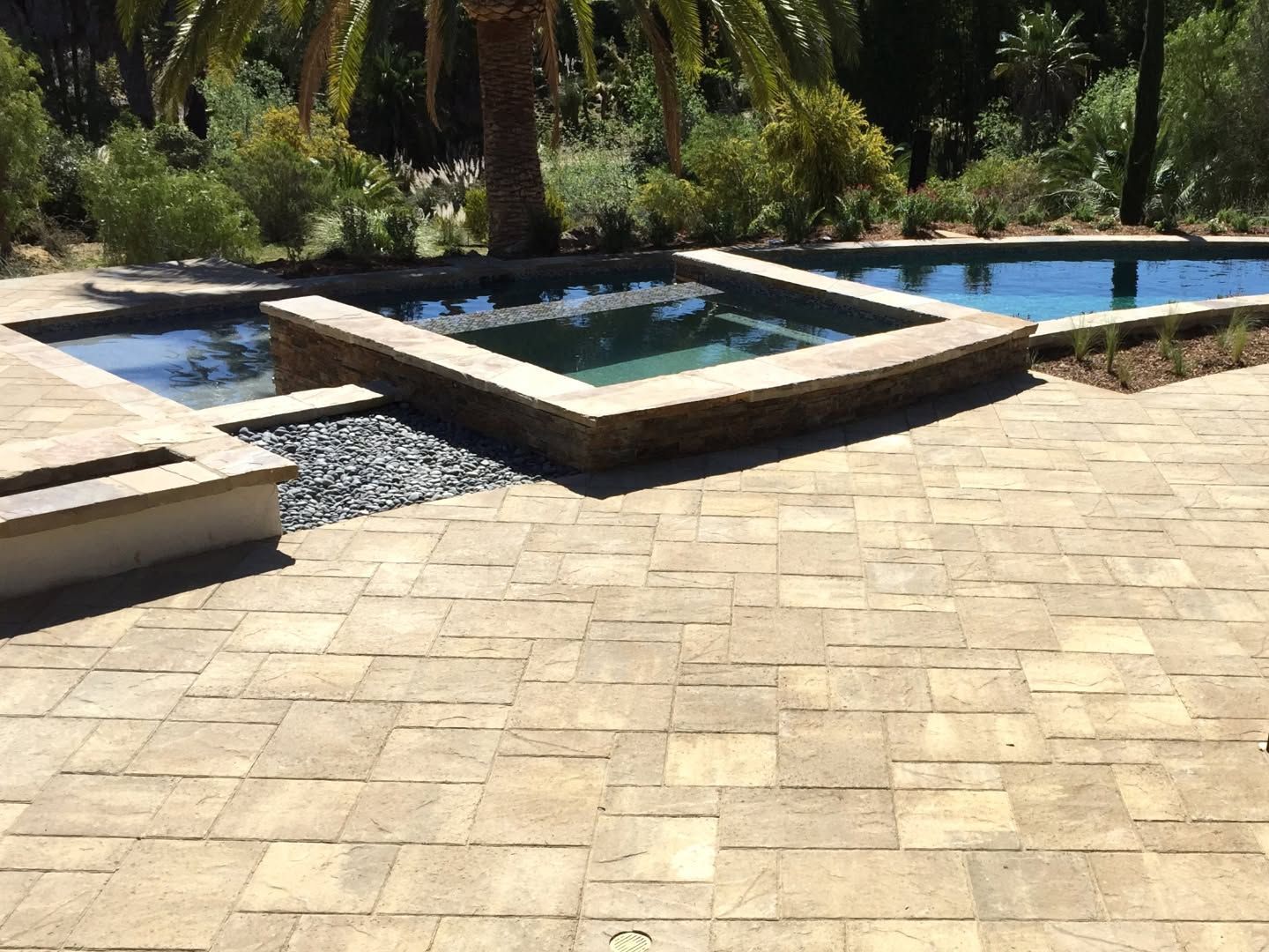 Stone patio with small rectangular pools and a surrounding garden in sunlight