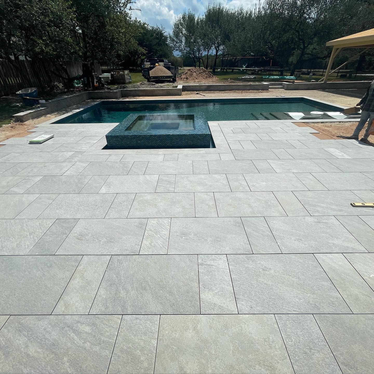 Modern backyard patio with a rectangular swimming pool, stone pavers, and trees in the background