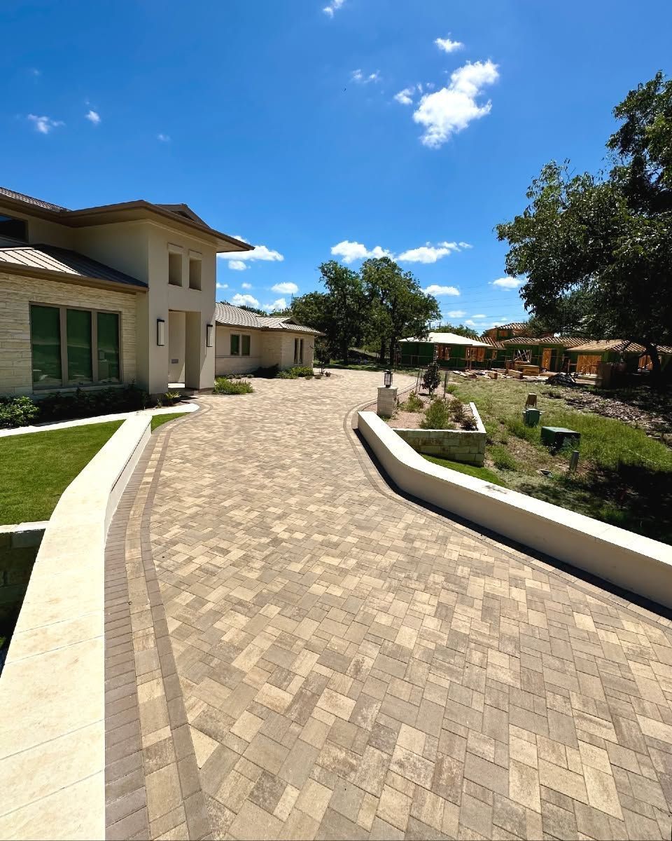 Curved brick walkway beside a beige building and landscaped garden under a bright blue sky
