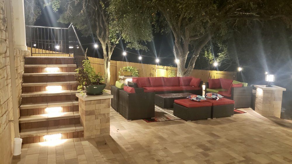Outdoor patio lounge with red and black sofas, lit steps, potted plants, and string lights at night