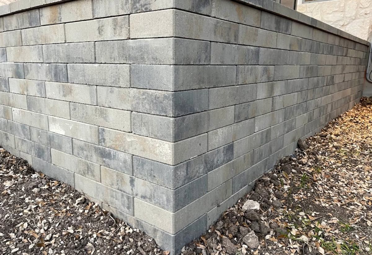 Gray cinder block wall corner with leaf-covered ground around it
