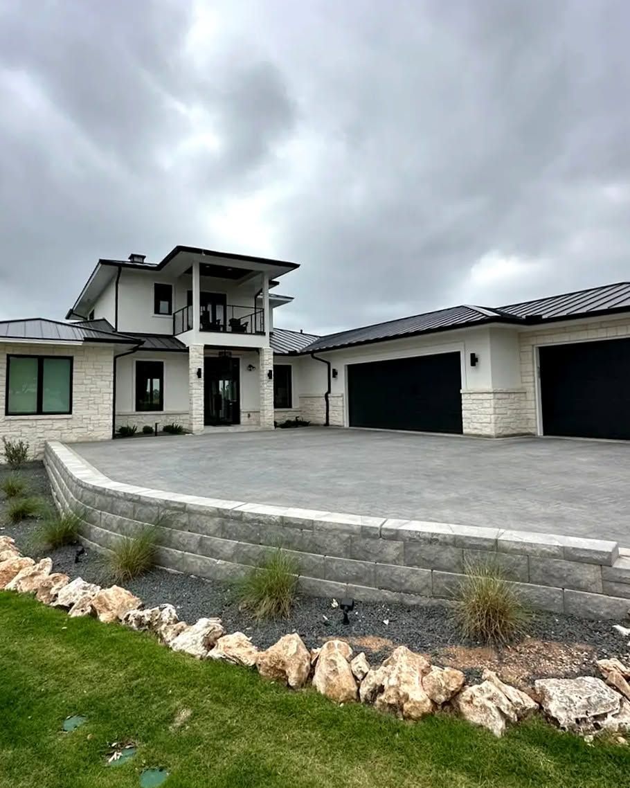 Modern two-story house with a stone facade, three-car garage, and cloudy sky over a curved driveway