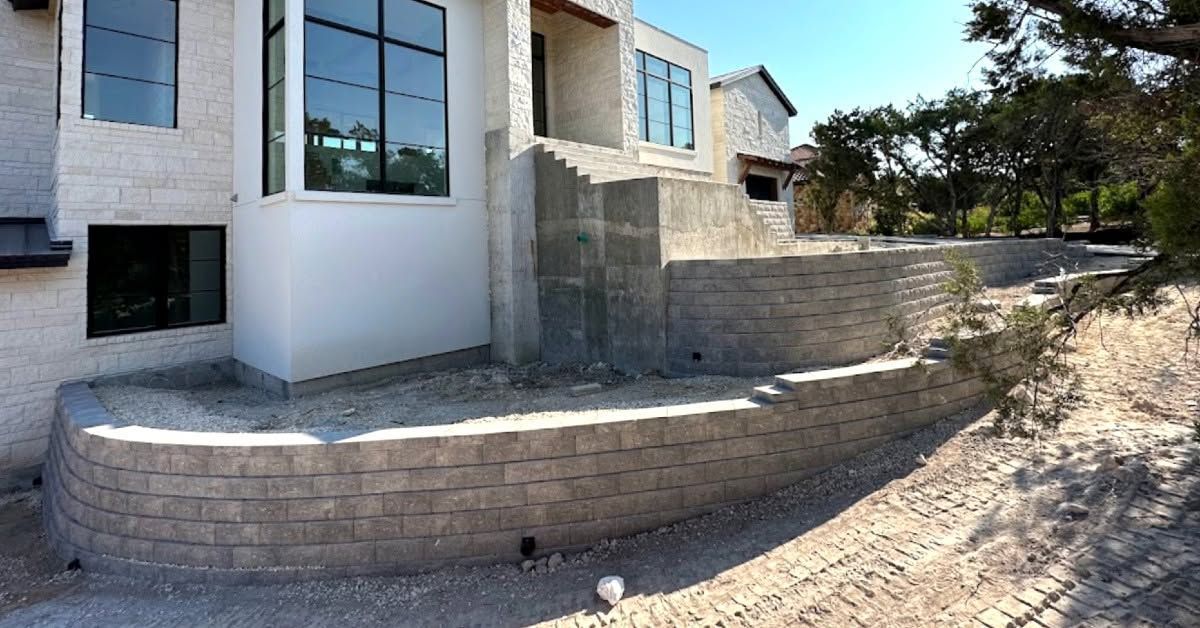 Stone retaining wall beside a modern house on a sloped, gravel yard