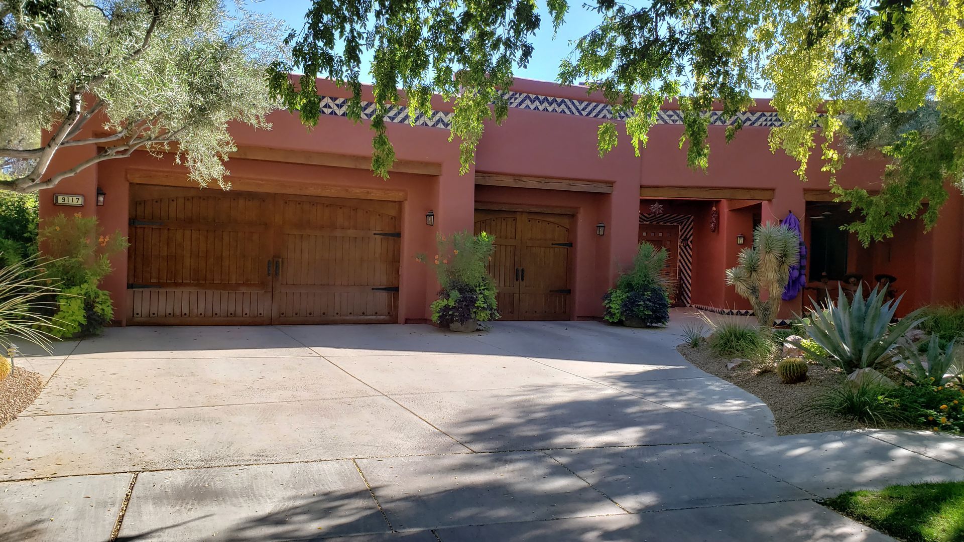 Red stucco home with three wooden garage doors, driveway, and landscaping.