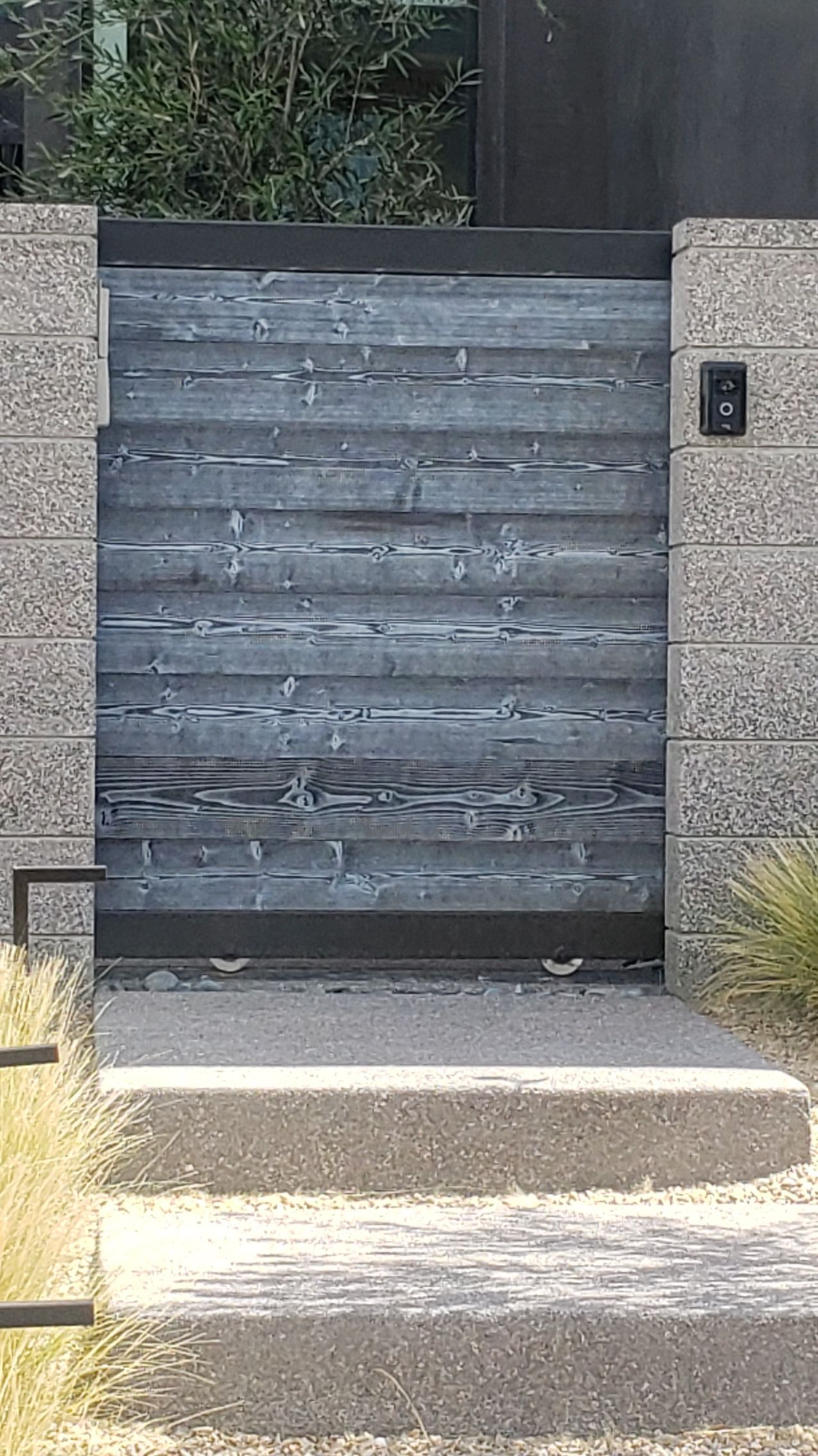 Gray wooden gate, mounted between stone pillars, with steps leading up.
