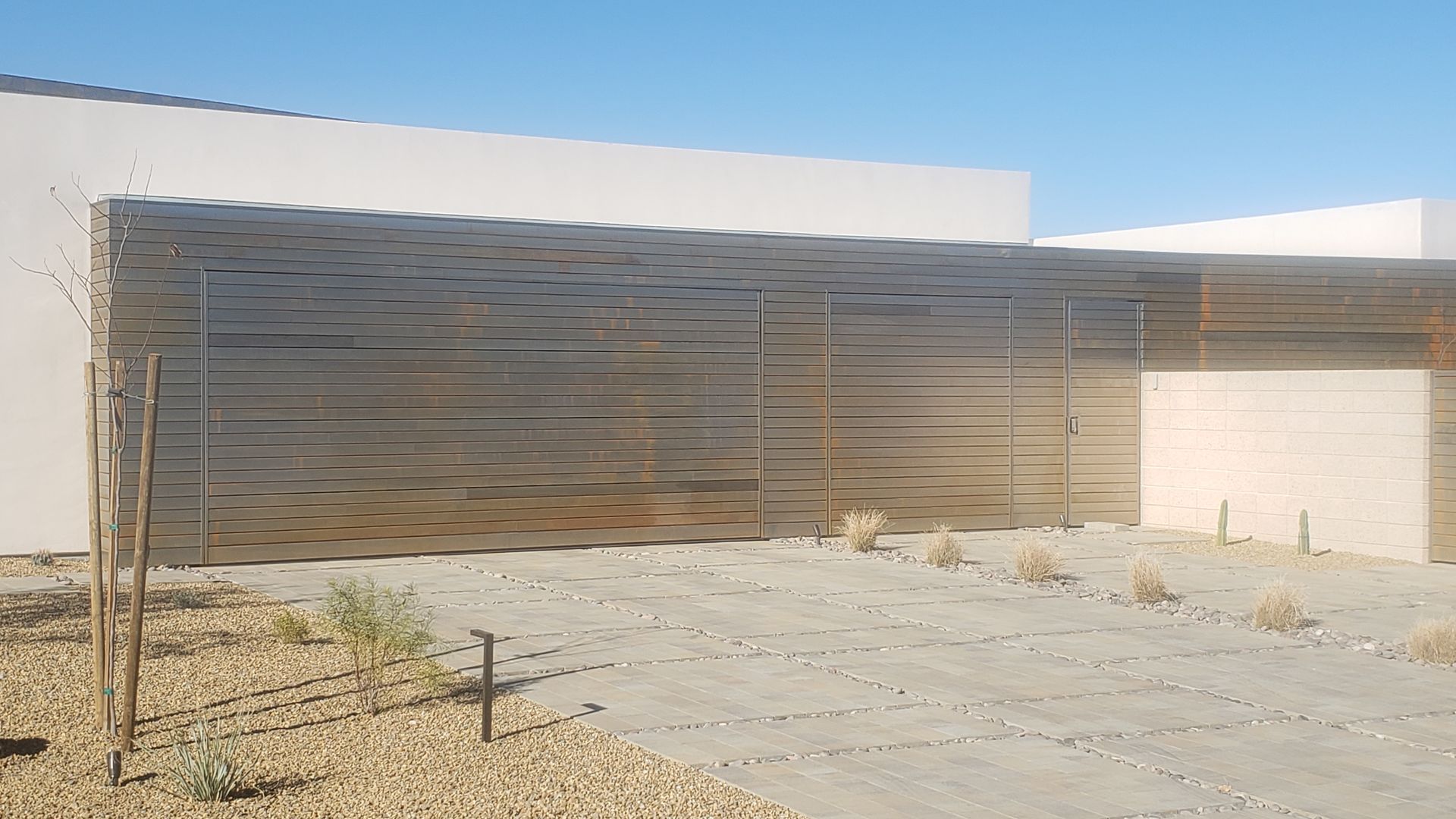 A modern home with a horizontal slatted metal fence in a desert landscape.