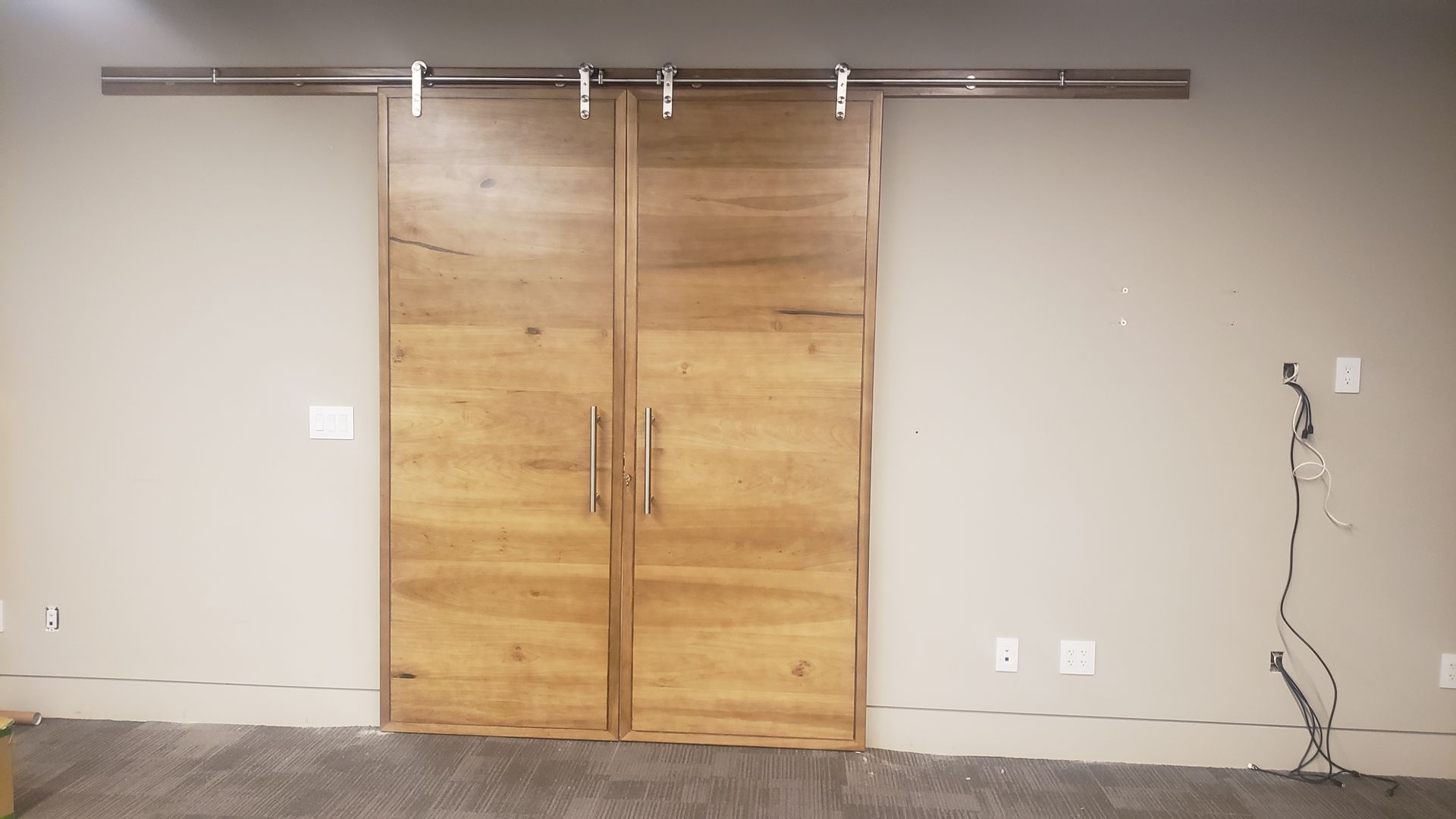 Double wooden barn doors on a wall, mounted with silver hardware.