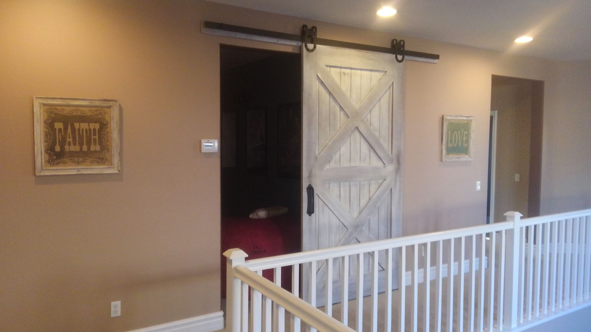 A wooden barn door on a second floor hallway, with a white railing and tan walls.
