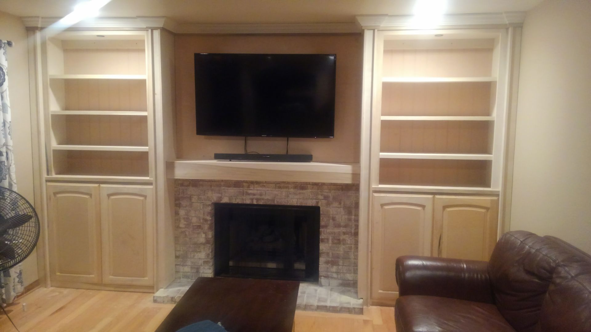 Fireplace with a mounted TV, flanked by bookshelves and cabinets. Brown brick and beige wood.