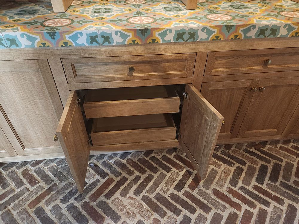 Wooden cabinet with open drawers, a patterned countertop, and brick flooring.