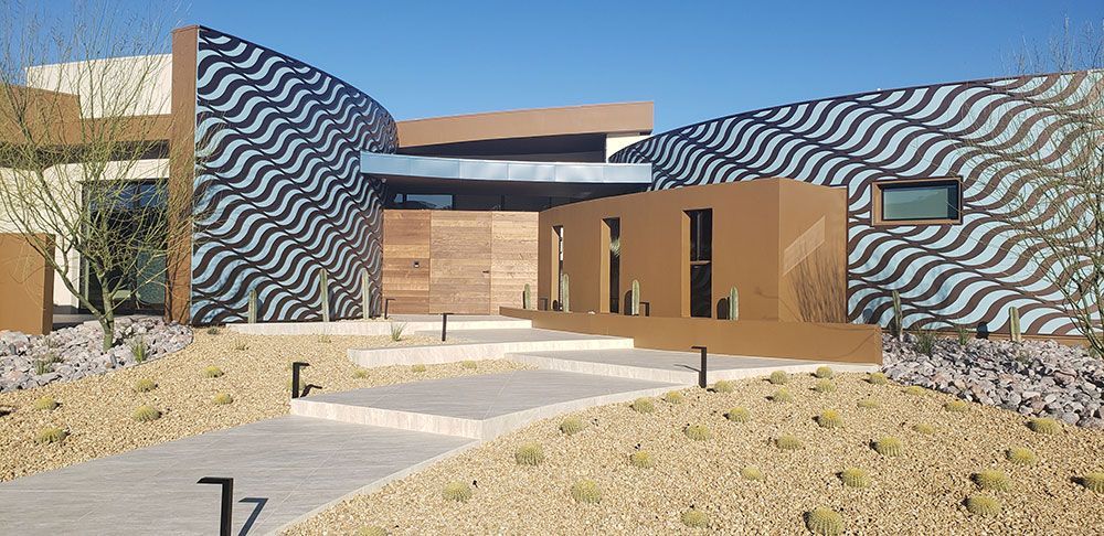 Modern building with patterned facade, pathway, and desert landscaping under a blue sky.