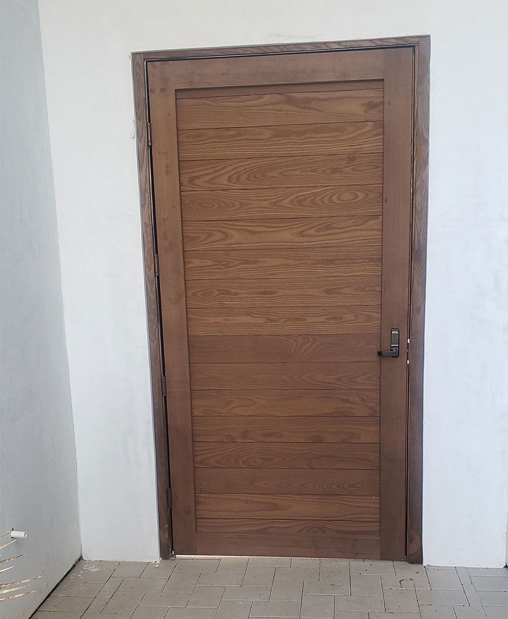 Brown wooden door set in a white wall, rectangular, with a dark frame, brick floor.