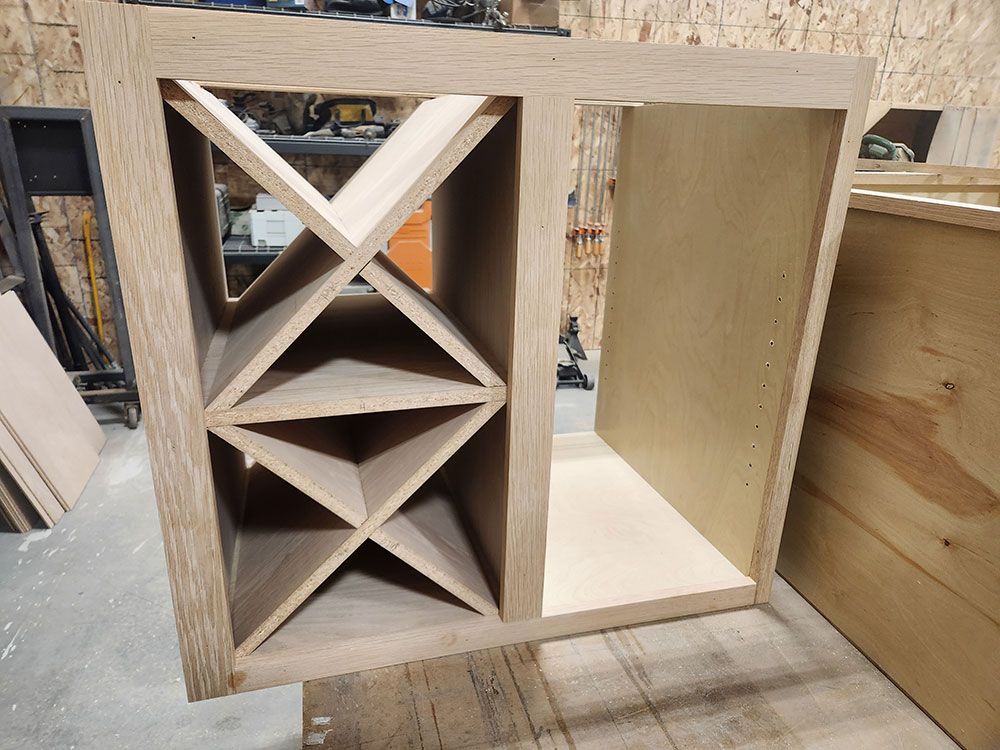 Wooden wine rack cabinet with angled dividers for bottles, beside an open storage space.