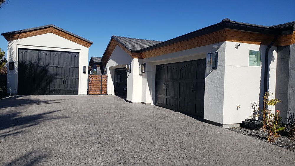 White house with black garage doors and brown trim under a blue sky.