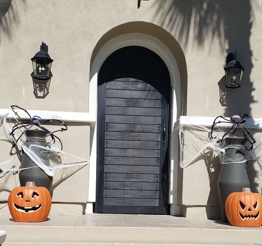 Halloween-decorated doorway with black door, pumpkins, spiders, and cobwebs.