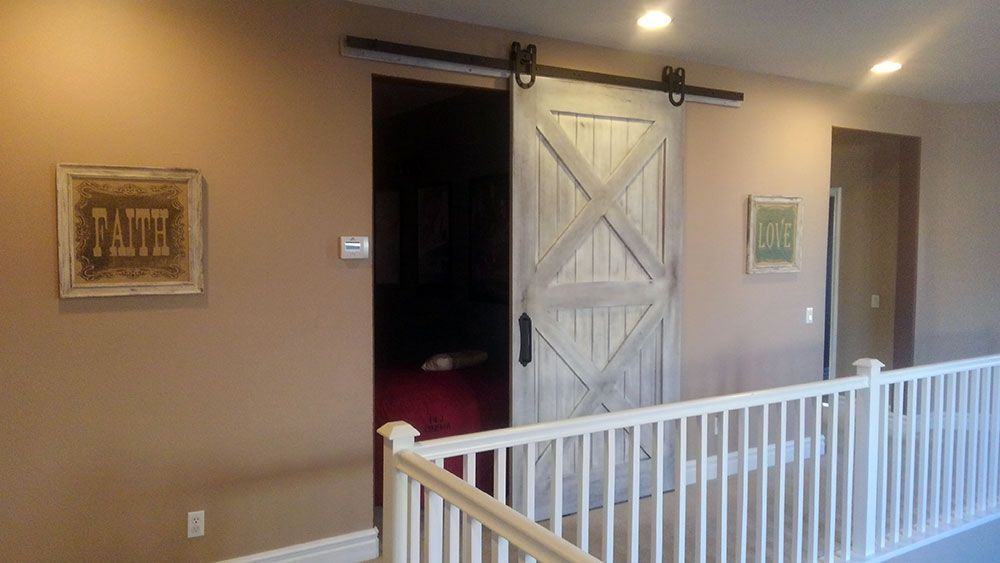 Barn door on a tan wall, white railing, two framed pictures, and overhead lights.