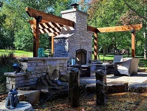 Outdoor stone fireplace with pergola and seating area.