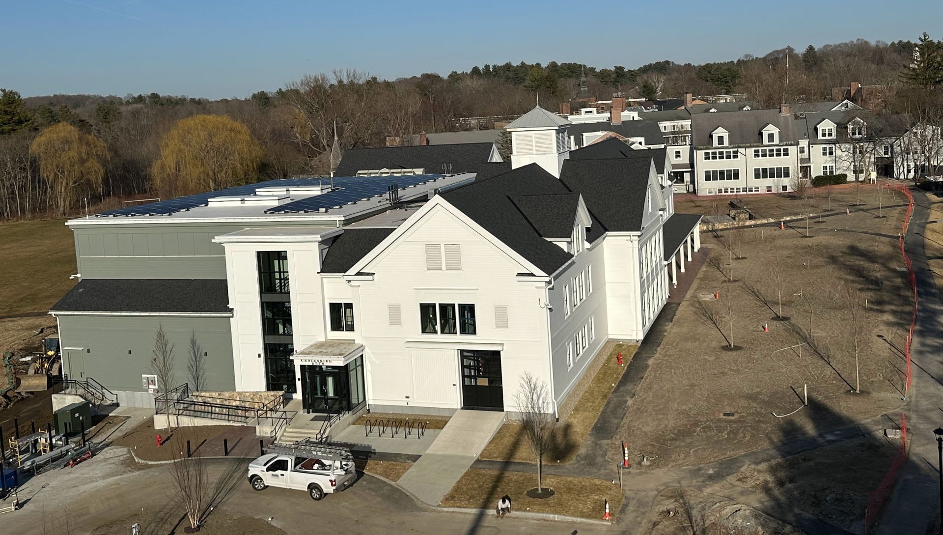 White multi-story building with solar panels on roof, in a cleared field, another building visible in the background.