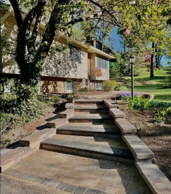 Stone fire pit and patio surrounded by a curved retaining wall and green grass.