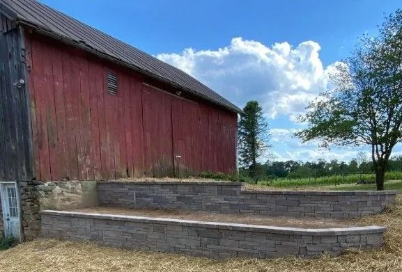 Red barn with gray stone tiered retaining wall; sunny day.