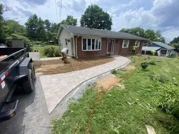 Workers building a concrete walkway to a brick house with a lush green lawn.