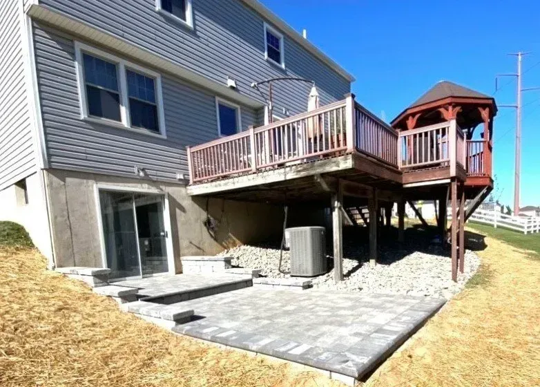Gray house with elevated deck, gazebo, patio, and dry landscaping under blue sky.