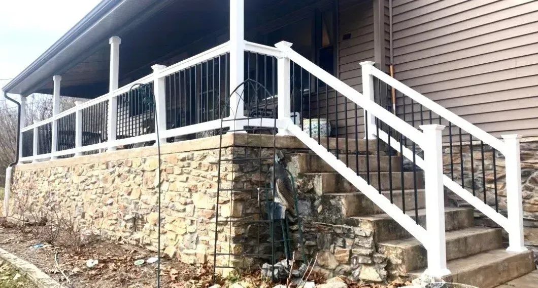 White and black railing with steps leading up to a porch with stone foundation.