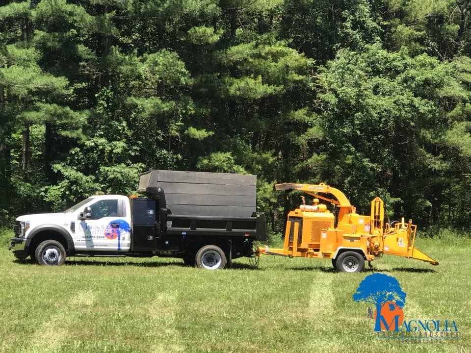 White truck towing a yellow wood chipper in a grassy field, trees in the background.