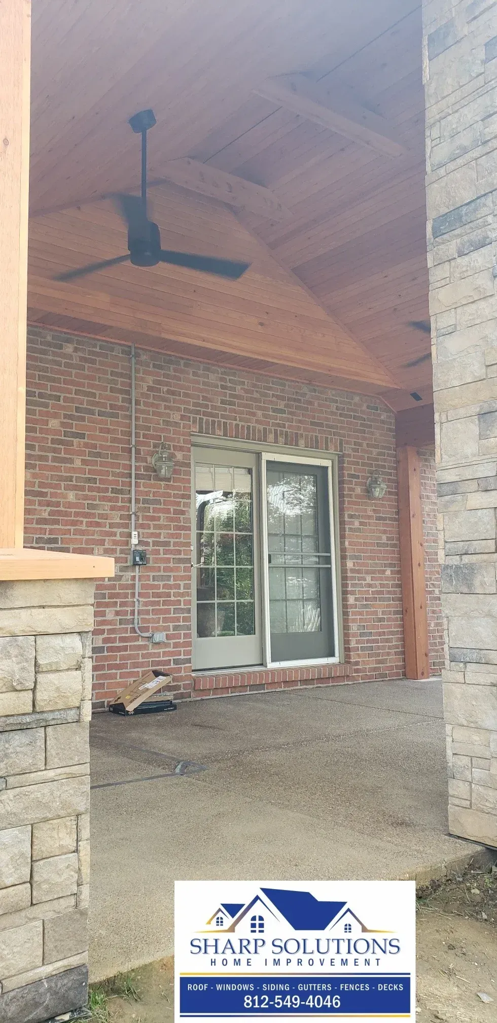 Covered brick porch with wood ceiling, ceiling fan, and glass double doors on a home exterior