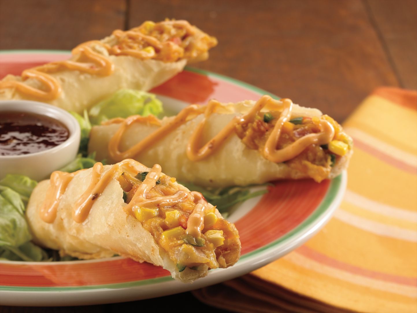 Flautas fried food rolls with sauce, garnished with lettuce, served on a plate with dipping sauce.