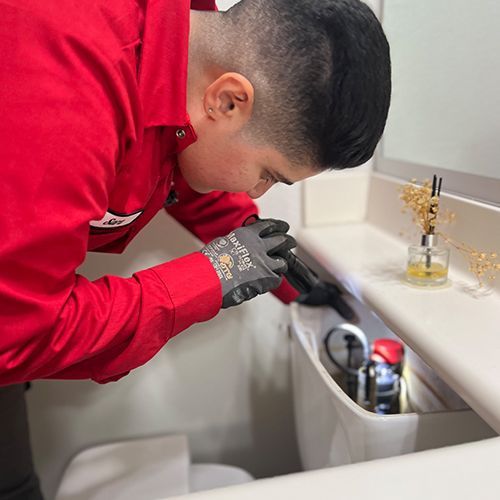 A person in a red shirt is fixing a toilet in a bathroom.