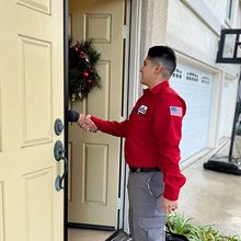 A person in a red shirt is shaking hands with person in a doorway.