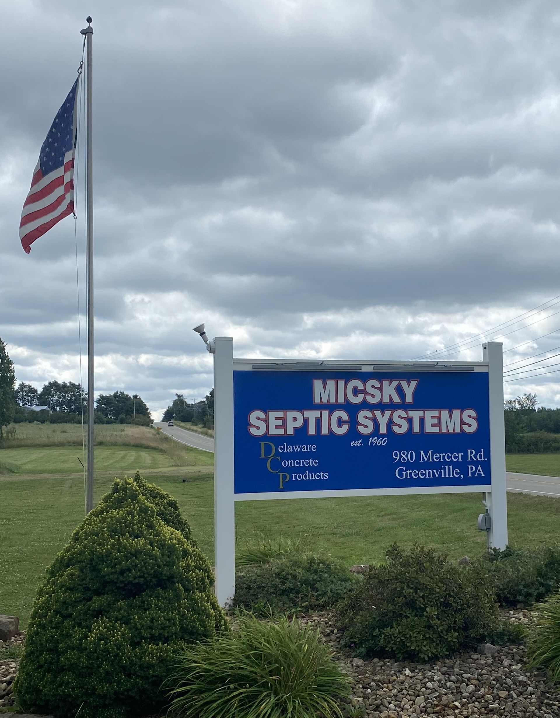 A blue sign for micsky septic systems with an american flag flying in the background.