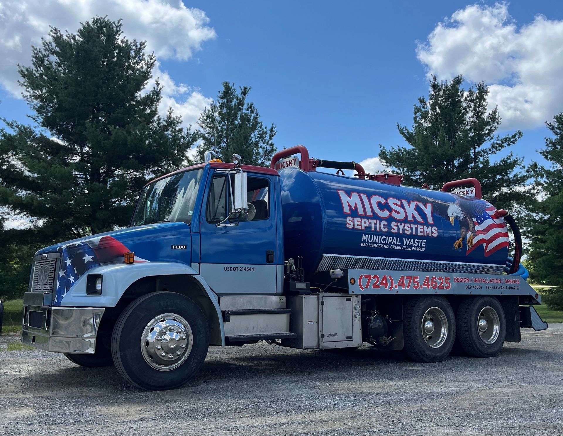 A blue and white septic system truck is parked in a gravel lot