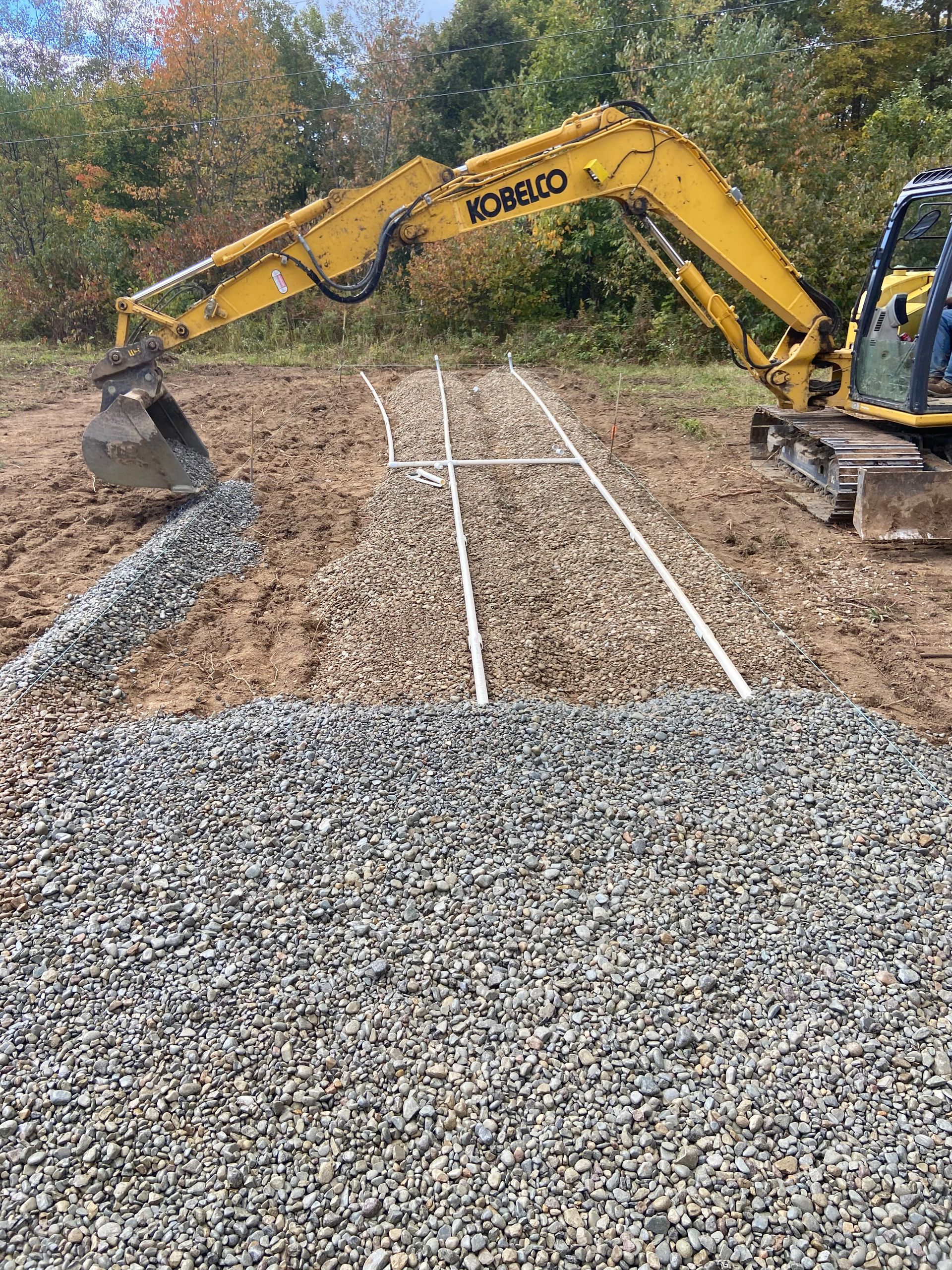 A yellow excavator is moving gravel in a field