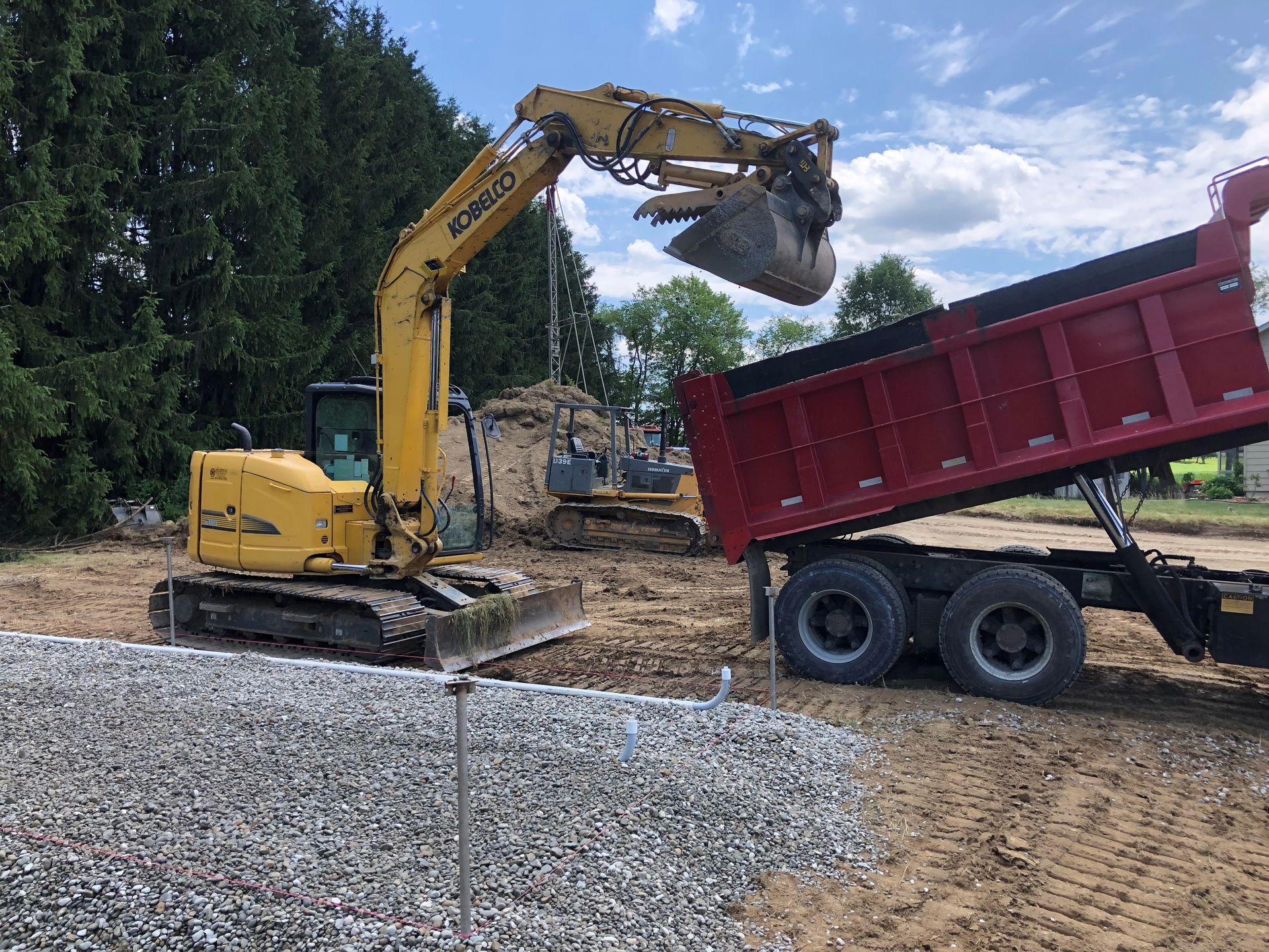 A yellow excavator is loading dirt into a red dump truck