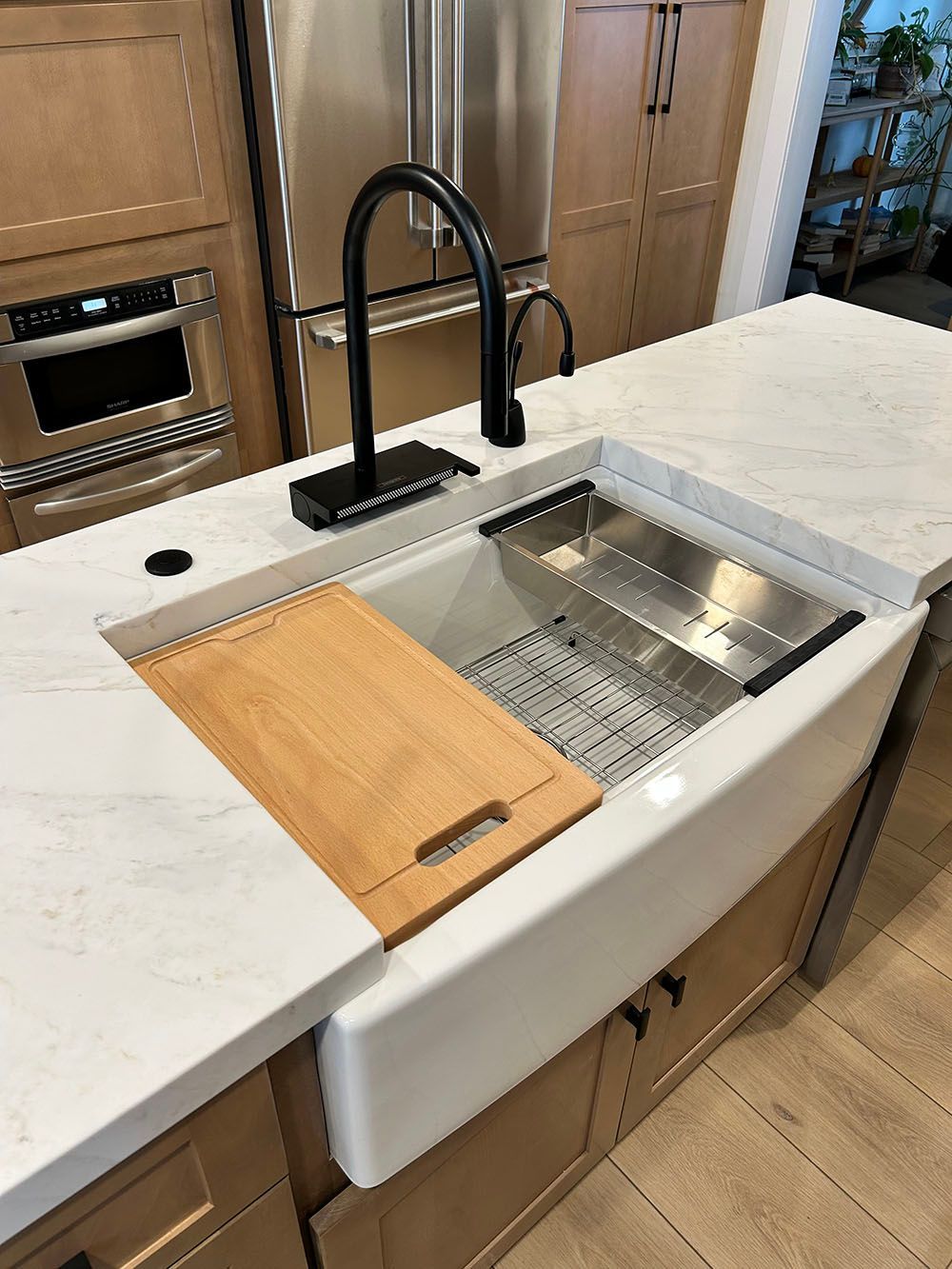 A kitchen sink with a wooden cutting board on top of it.