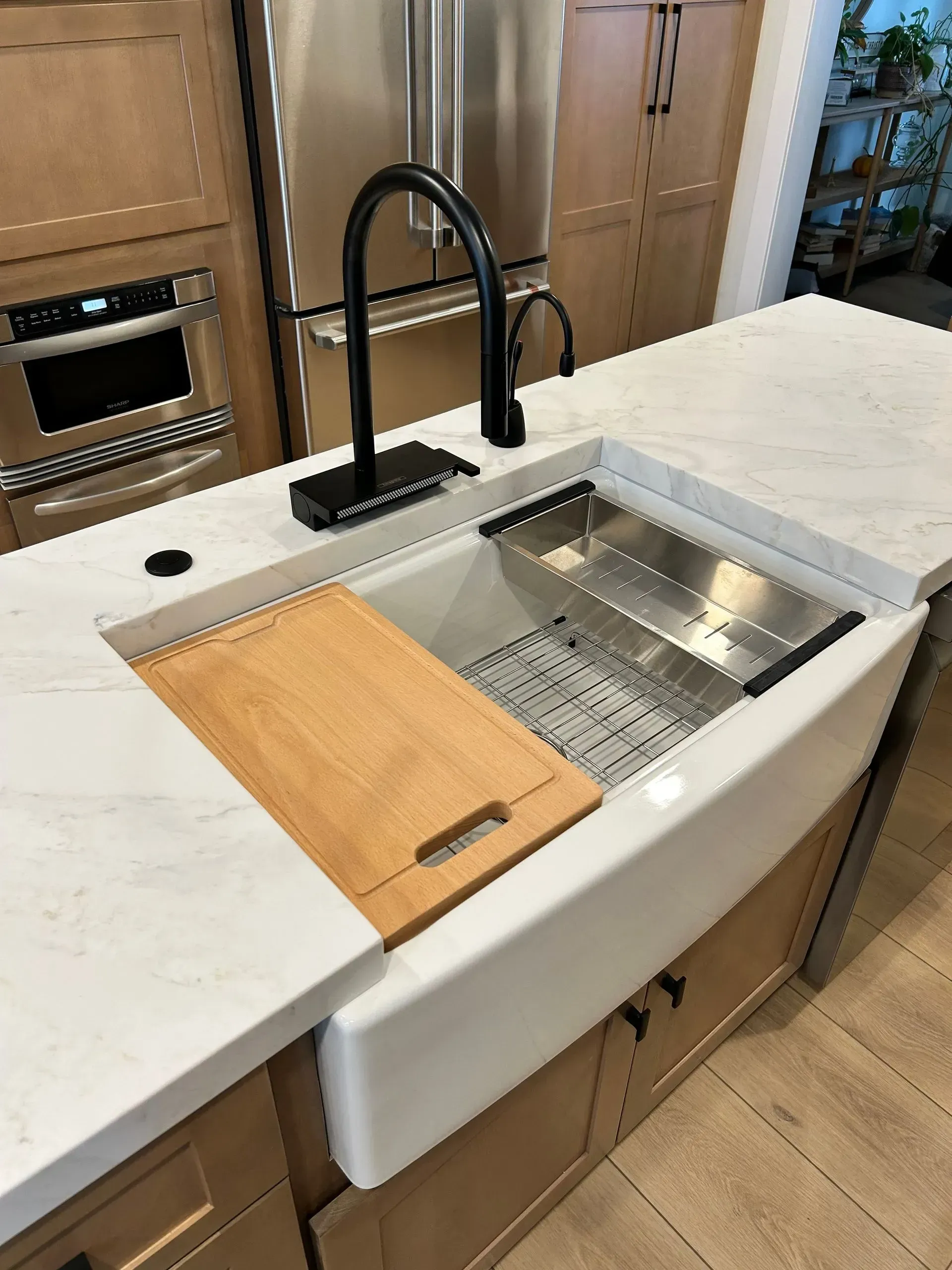 A kitchen sink with a wooden cutting board on top of it.