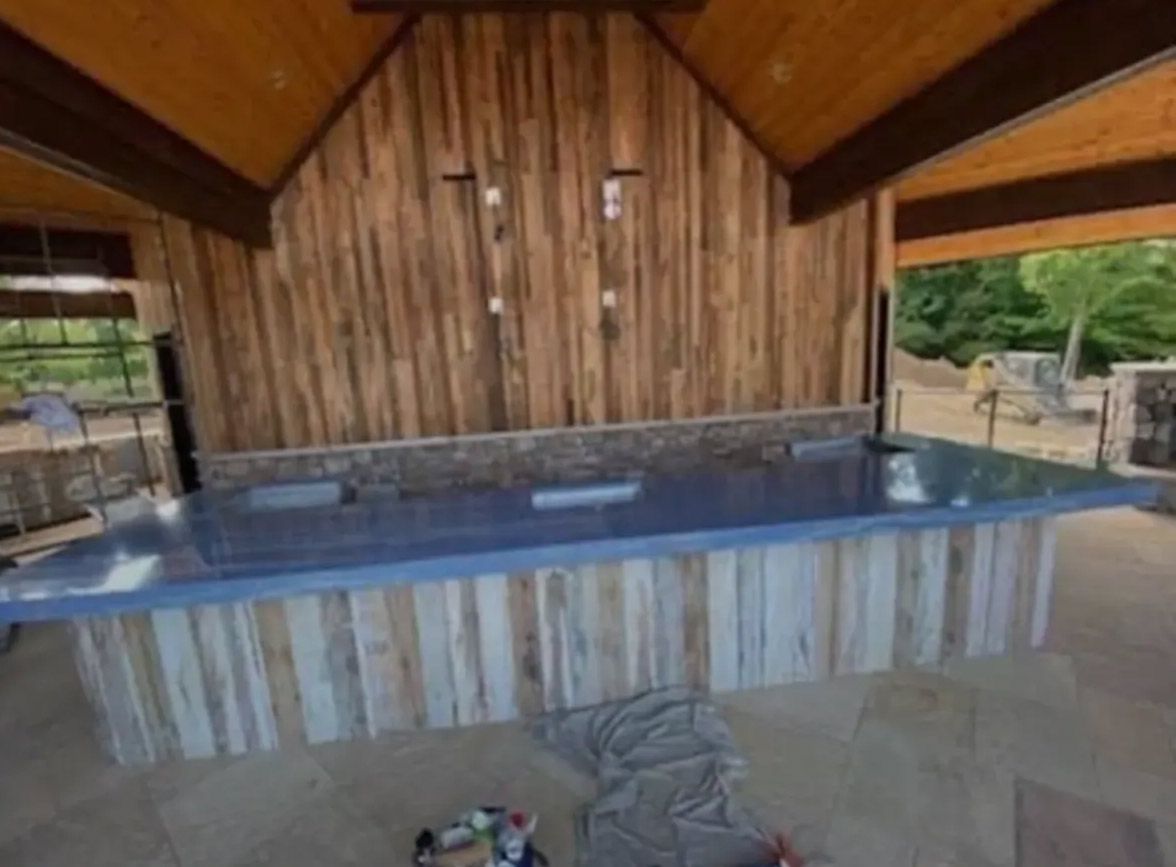 A hot tub is sitting under a wooden roof in a gazebo.