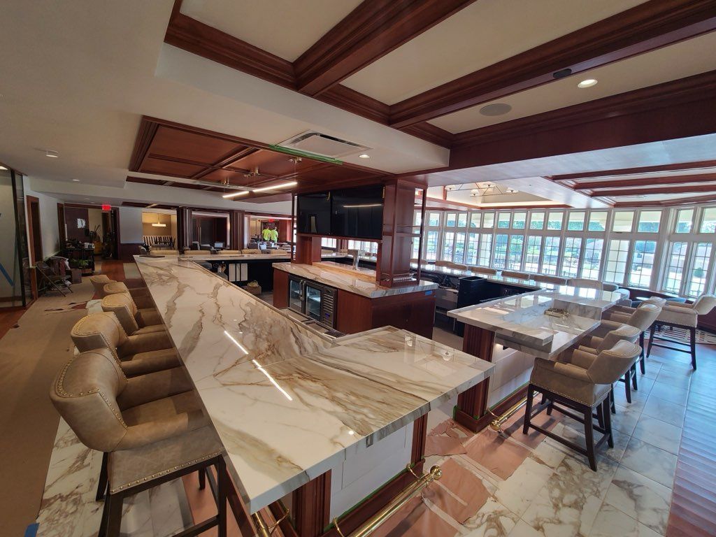 Long bar and dining area with marble counters, wooden accents, and large windows.