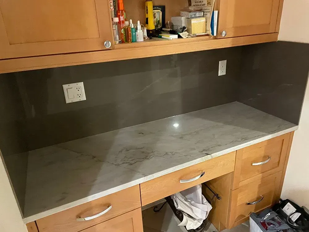 A kitchen counter with a gray counter top and wooden cabinets.