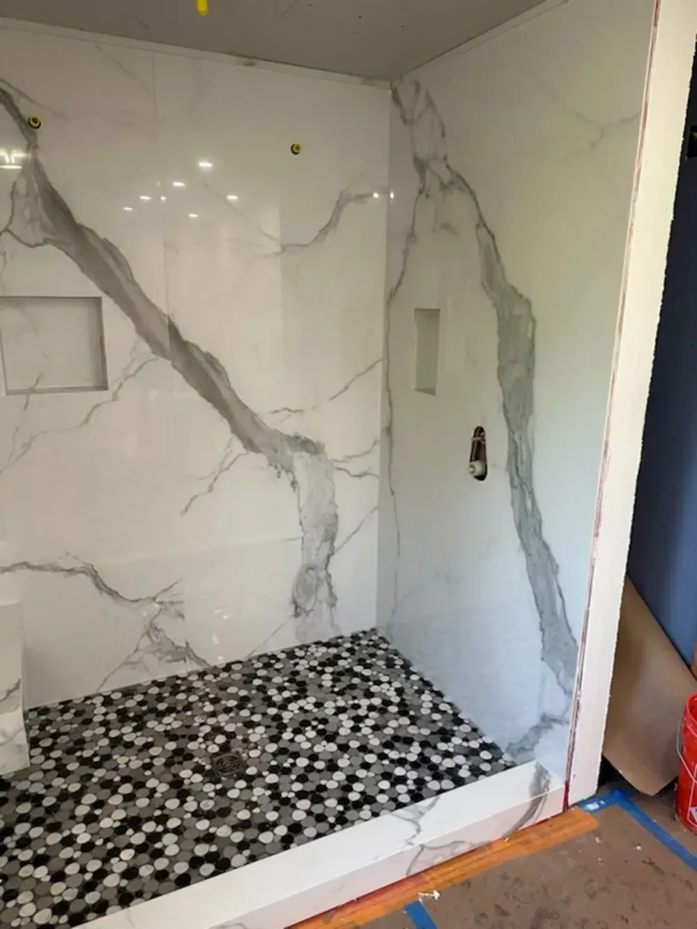 A shower with marble walls and a black and white tile floor.