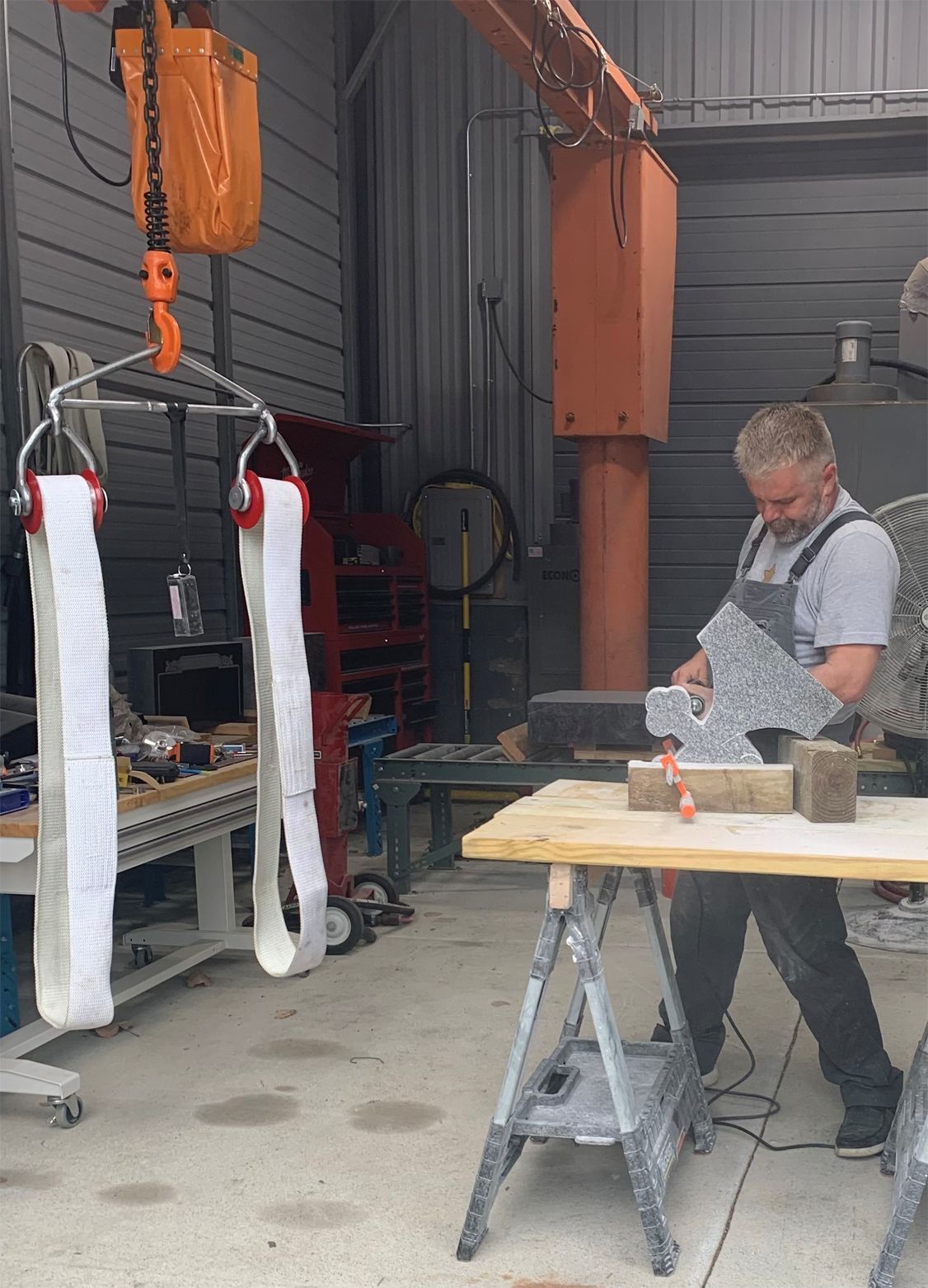 Man working on stone sculpture in workshop, lift in background.