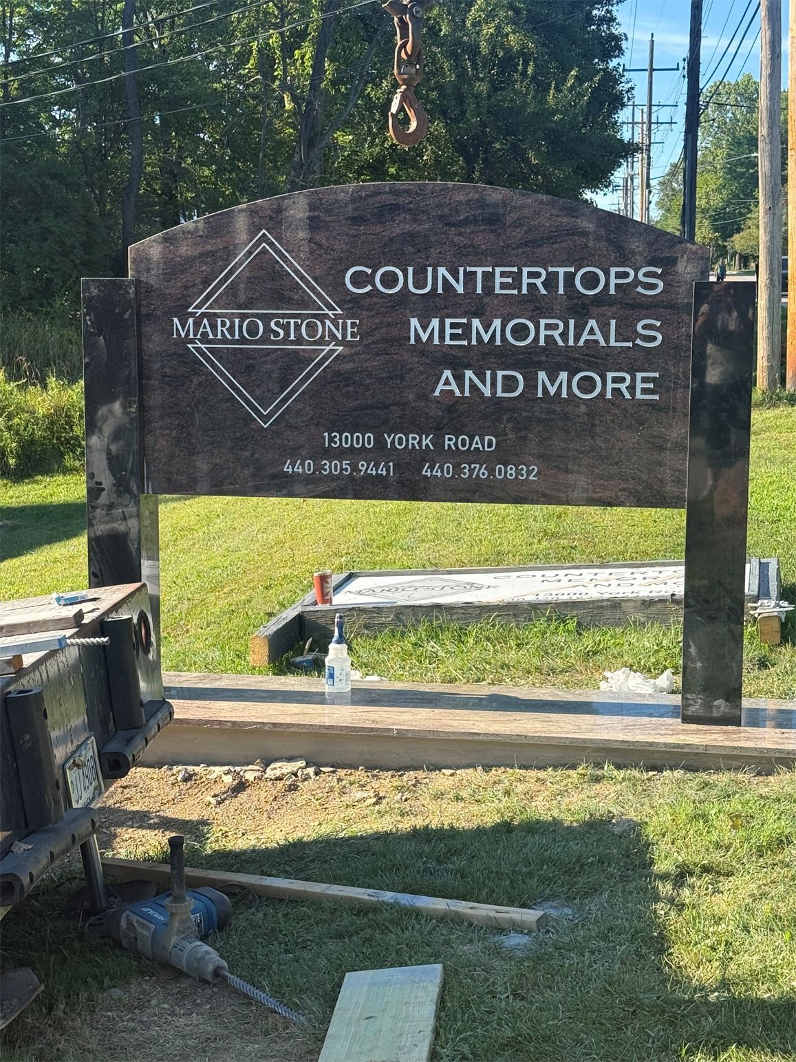 Mario Stone sign being installed; weathered wood, green grass, sky in background.