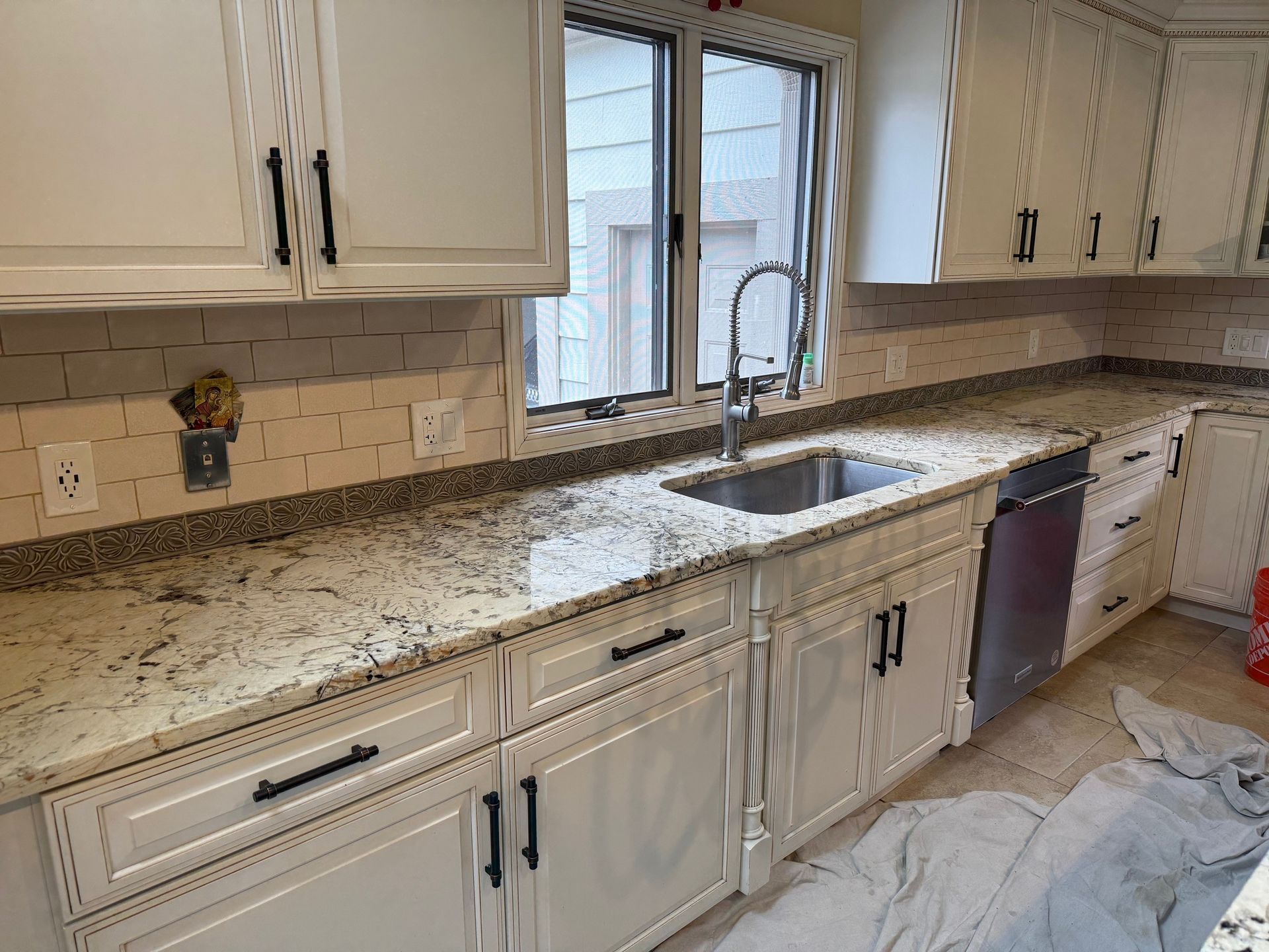 A kitchen with white cabinets, granite countertops, a sink, and a window.