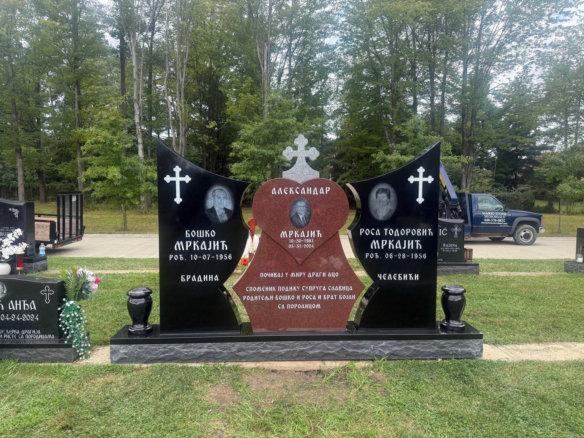 Black and red granite headstone in a cemetery. Includes photos and text with cross.